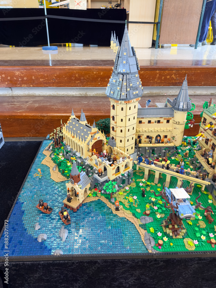 Fototapeta premium Side view of a massive custom LEGO Hogwarts Castle diorama featuring the Great Hall, students in boats on a blue brick water surface, and the Whomping Willow with a car: 06.10.2024-Ljubljana, Slovenia