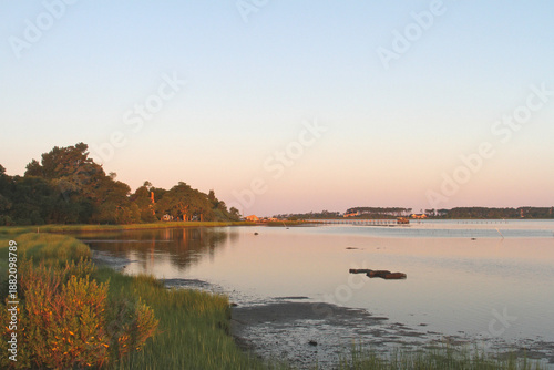 Fotografia A peaceful Chesapeake Bay morning with warm sunrise light reflecting across calm water, marsh grasses, and distant shoreline trees