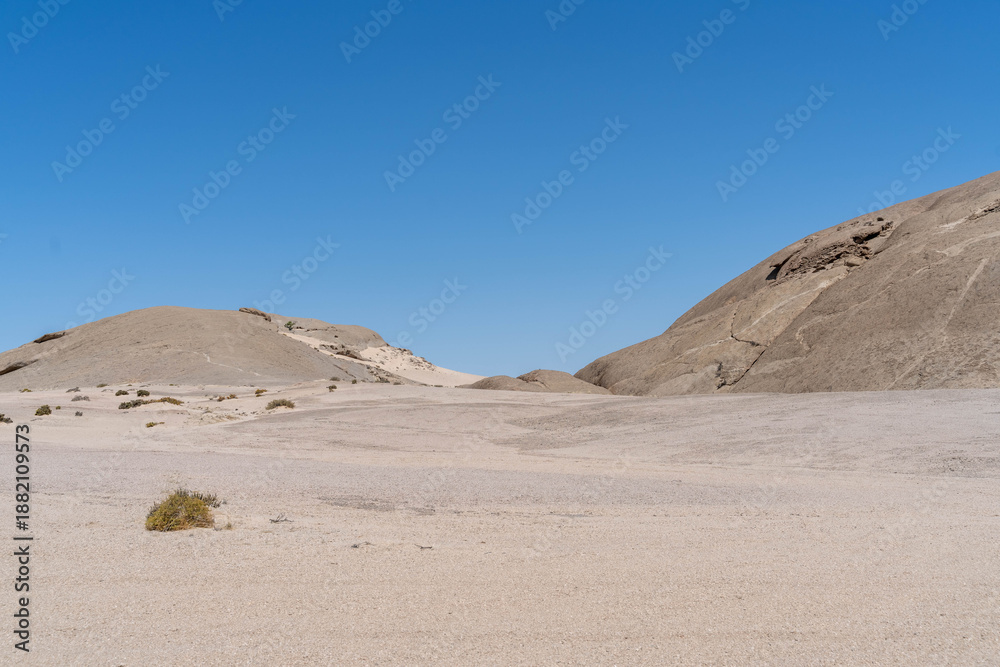 Fototapeta premium On the way to Swakopmund, an endless road stretches through the striking landscape of the Namib Desert. Vast open plains, arid terrain, and gentle sand dunes meet a wide, dramatic sky.