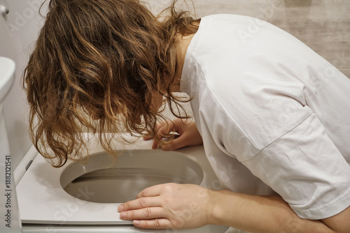 Woman experiencing sickness and stomach pain, leaning over toilet bowl