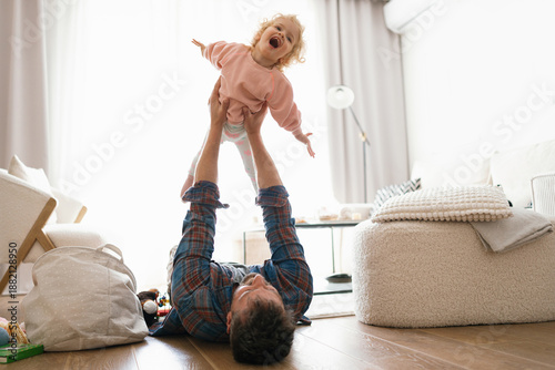 Фотография Father Lying on Floor Lifting Toddler Daughter Pretending to Fly