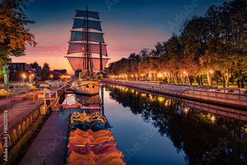 Illuminated morning view of docked sailboat on Danes river. Exciting summer cityscape of Klaipeda town, Lithuania, Europe. Stunning daw on the river. Traveling concept background.