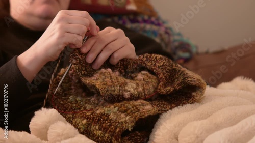 Person knitting a scarf out of handspun yarn.  Close up view of hands knitting a warm wool scarf, while on the couch.