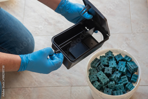 Close up of exterminator hands in blue gloves opening a rodent bait station box