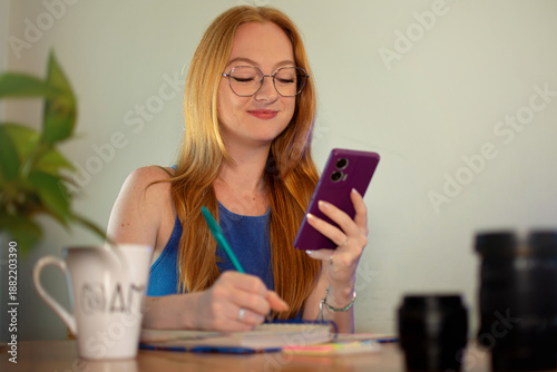 mulher mexendo no celular e fazendo anotações no papel, uso de redes sociais de pessoas jovens