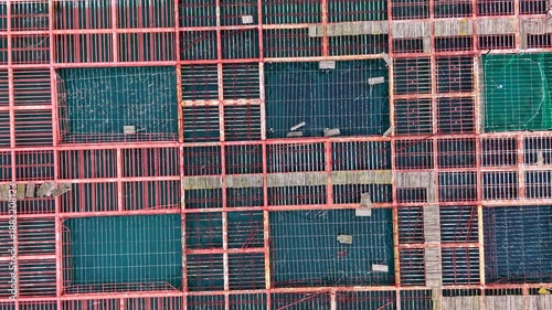 Rows of nets and containers are set up in the sea for mussel farming. Workers may be present tending to the harvest. Bright sunlight illuminates the clear water.