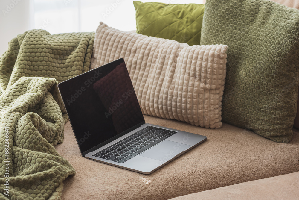 Fototapeta premium Laptop on Cozy Sofa with Textured Pillows and Blanket. Relaxed Home Workspace