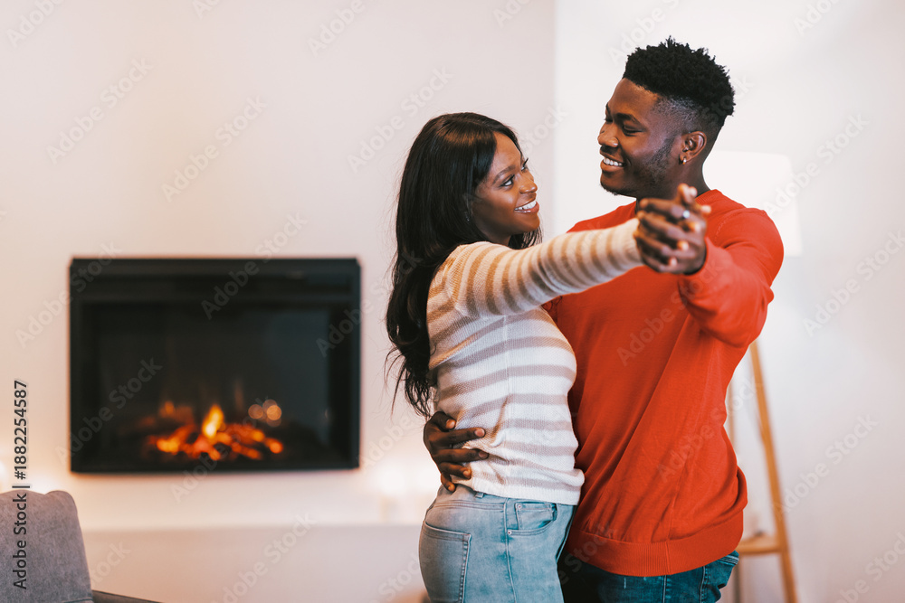 Fototapeta premium A couple enjoys a moment of dancing in a warm room. They smile at each other while holding hands. The fireplace adds warmth to their interaction during the evening.