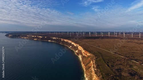 Wallpaper Mural A view of many wind turbines along a cliff edge next to the sea. The sun is out and the sky is blue with some clouds. The land is flat and stretches far into the background. Torontodigital.ca
