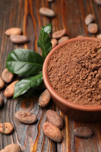 Natural cocoa beans, powder and green leaves on wooden table, closeup