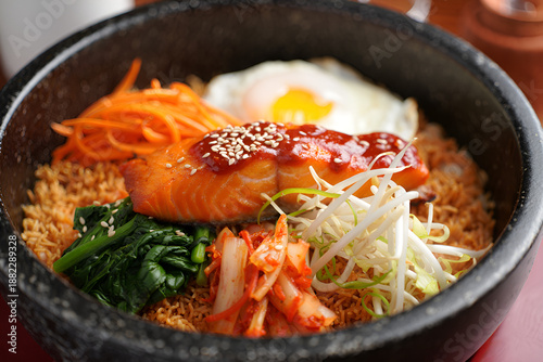 Korean bibimbap with salmon, fried egg, and fresh vegetables in a stone bowl