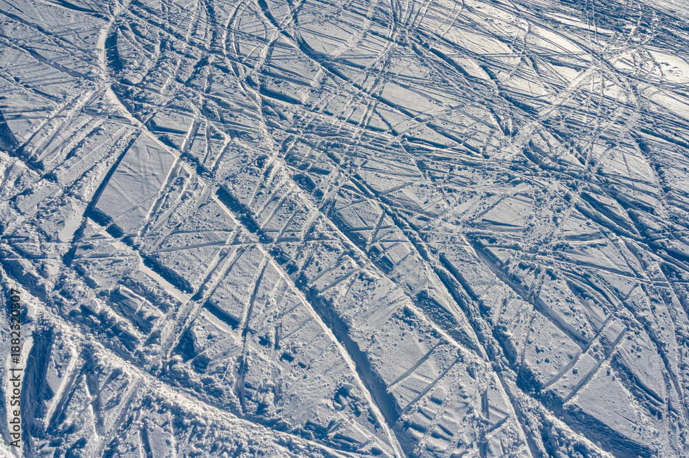Fototapeta premium Aerial top view of messy ski and snowboard tracks on a white snow slope. Abstract winter texture of mountain resort trail, active lifestyle and sports background