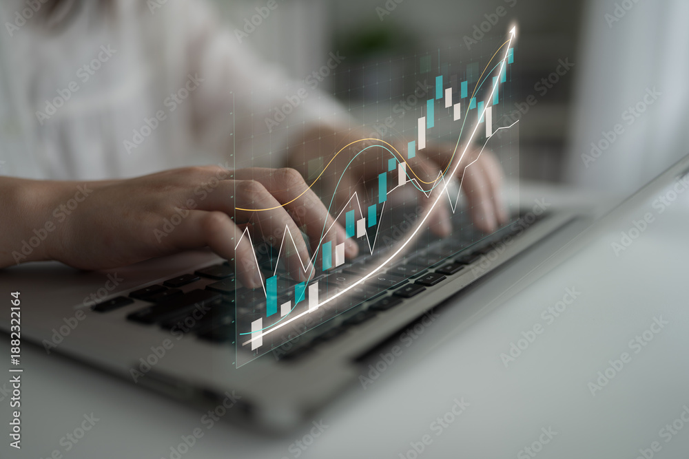 Fototapeta premium Hands typing on a laptop with a digital financial graph overlay, illustrating the concept of data analysis and investment growth in a modern business environment. Impute