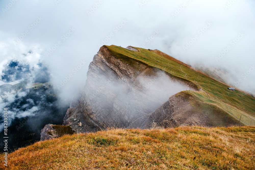Fototapeta premium Seceda mountain ridge in the Dolomites shrouded in atmospheric mist and clouds