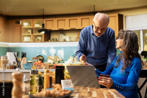 Quadro em tela Senior couple doing online shopping with a debit card together, reviewing groceries and daily essentials in e-commerce app on laptop