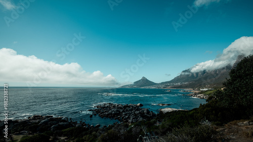 panoramic view from Lion's Head overlooking Camps Bay and the Twelve Apostles mountain range in Cape Town, South Africa. The turquoise Atlantic Ocean meets the white sands of Camps Bay beach, framed