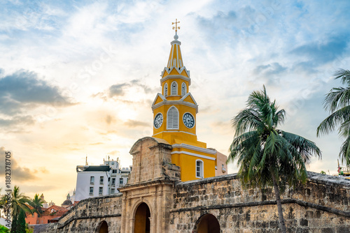 Sunset view of Torre del Reloj in Cartagena, Colombia highlights warm tropical light over stone colonial walls and palm trees. The soft sky and golden hour tones the historic atmosphere of location