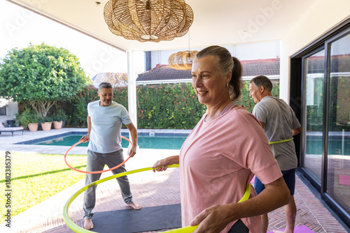 Photos Senior friends exercising with hula hoops on tiled patio by pool, woman wearing
