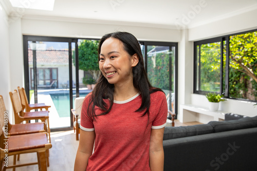 Free Download Adult Asian woman smiling and standing in living room wearing red tee, sliding doors showing pool - GFXLoad