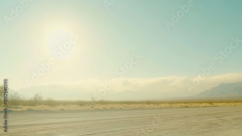 Dust clouds gather on the horizon under a hazy bright sky over a vast open landscape with a dirt road in the foreground
