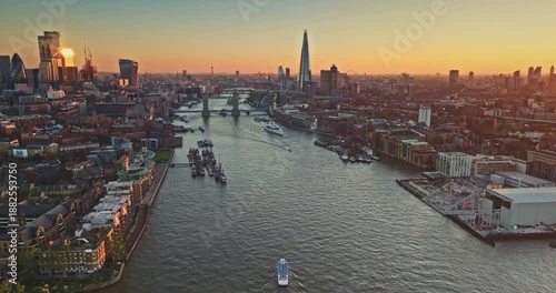 England, London skyline at sunset, River Thames winding past Tower Bridge and The Shard, blending historic landmarks and modern urban cityscape architecture in golden evening glow. Aerial view flight