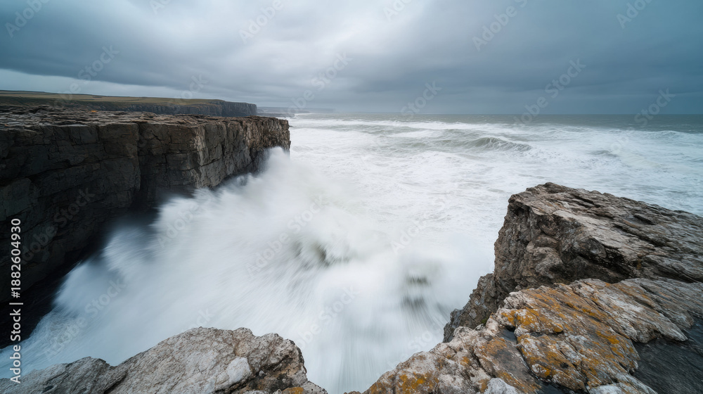 Fototapeta premium Dramatic rocky coastline with huge waves crashing against cliffs under cloudy sky creating powerful and moody ocean scene