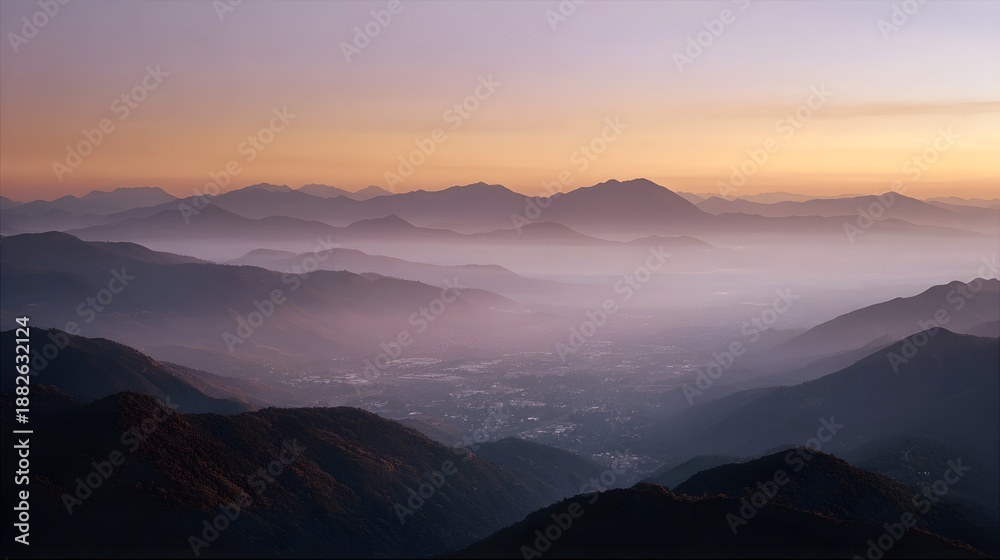 Fototapeta premium Layered mountain ranges shrouded in mist at sunset with a valley below
