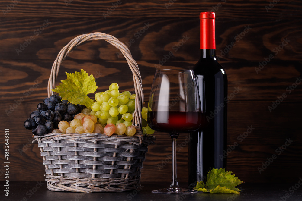 Fototapeta premium Red wine bottle with a glass and basket of fresh grapes