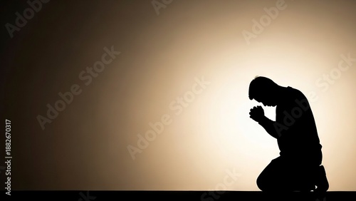 A silhouette of a kneeling person with hands clasped in prayer against a bright diffused light backdrop
