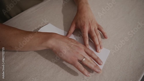 Medium top-down shot showing an adult man carefully folding a paper airplane on a table. Camera captures calm movements and step-by-step paper folding. High quality 4k footage