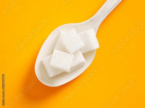 Photography Spoonful of white sugar cubes on orange background