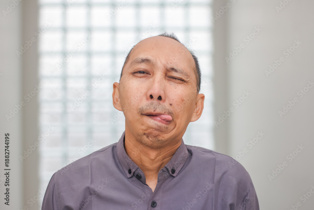 Fototapeta premium Playful Asian Man Winking with Tongue Out Funny Facial Expression