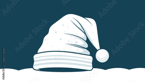 White winter hat with a pompom placed on top of a snow hill against a dark blue background during the holidays.