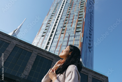 Photos Woman gazing up at a towering glass skyscraper in a modern city, urban architect