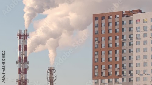 Thermal power plant pipes with vapor rising to the sky near the new residential building. Vapor rising in front of the blue sunny sky.