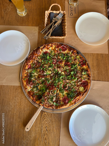 Freshly baked pizza topped with herbs, meat, and melted cheese is served on a wooden table