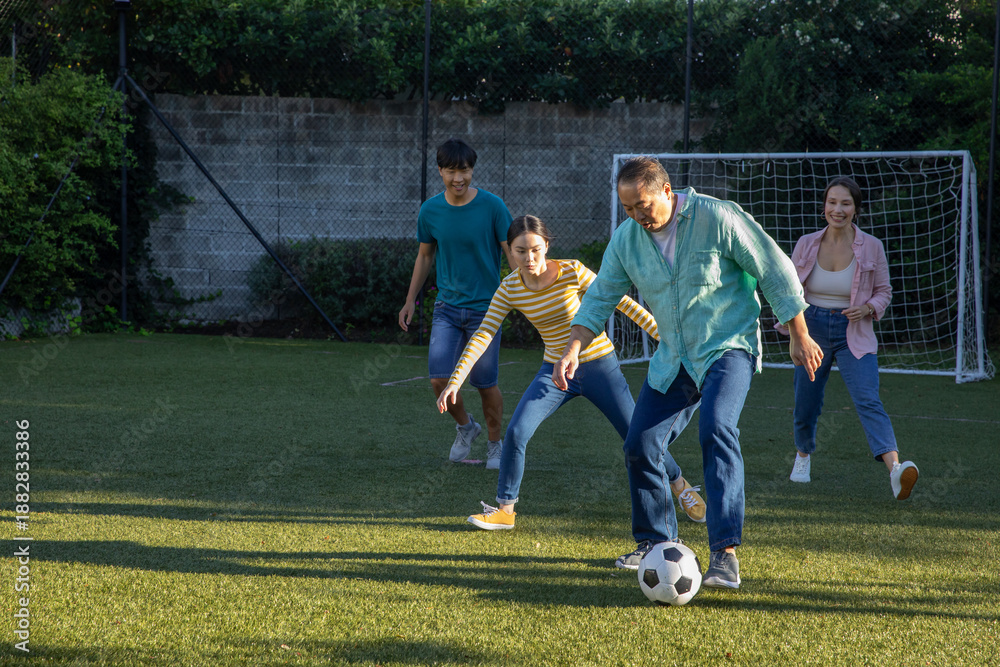 Obraz premium Diverse family playing soccer on grass field next to brick wall with soccer ball and goal net
