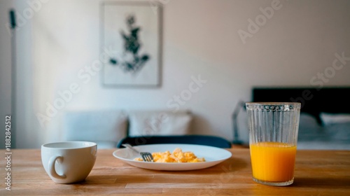 Simple home breakfast table with coffee, plate of food and orange juice in a minimalist interior, natural morning light, cozy lifestyle still life at home