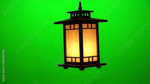 Traditional dark wood hanging lantern illuminates softly with a warm amber glow isolated against a vibrant chroma key green screen background for easy video editing applications