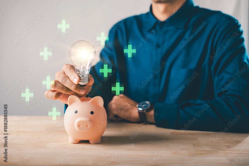 Fototapeta premium Financial innovation idea for piggy bank money energy investment saving, man holding glowing lightbulb helps save retirement finance growth with green positive plus signs around
