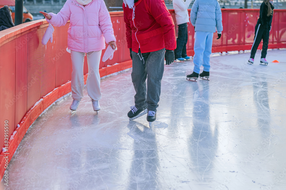 Naklejka premium Two people at the edge of skating rink barrier. Man coach in red and woman in pink, beginner skater. Ice skating on ice rink arena with people. Concept of sport support, winter sport, health, hobby