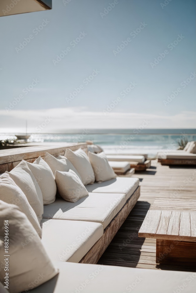 Fototapeta premium Sunlit beachside deck with cream cushions and wooden tables, overlooking the calm ocean. Concept Beachside deck, Sunlit atmosphere, Cream cushions, Wooden tables, Calm ocean view