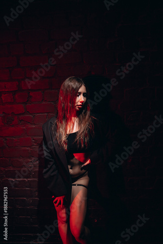 Принти на полотні Woman in a dark setting with red light wearing a black top and jacket