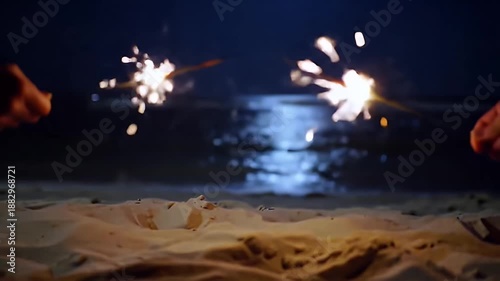 Sparklers Ignite The Night Sky Above A Sandy Beach With Soft Ocean Waves And Moonlit Reflections
