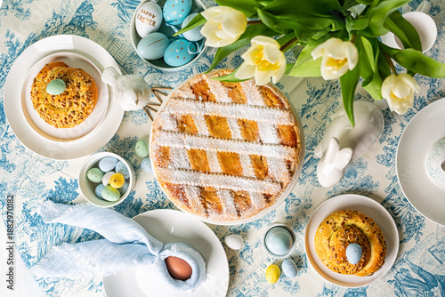 Served Easter round dining table directly above, Italian Easter cake, shortcrust pie with ricotta cheese, Pastiera Napoletana, colorful eggs, buns, easter bunny and bird sculptures,  tulips flowers. 