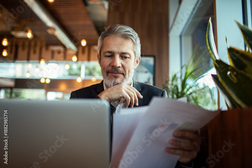 Mature businessman reviewing documents on laptop in cafe