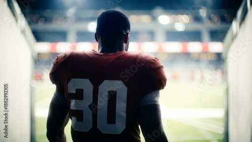 Rear view of an American football player walking through a stadium tunnel toward the field lights, professional athlete focus and preparation for championship game