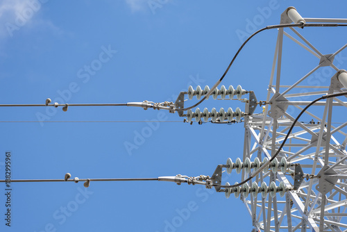 Schilderij op canvas Low angle close-up of electrical transmission tower's insulators, fittings, and other components connecting high-voltage power lines to the large metal lattice tower
