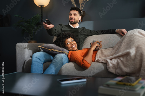 Foto Relaxed couple lying on sofa together, watching television online show at night