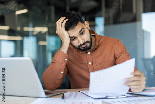 Foto Young male employee feeling tired and frustrated while looking at financial pape